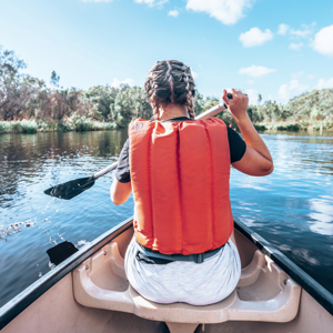 A Contiki travellers paddles a canoe across calm waters, surrounded by native bushland and mirrored reflections in the peaceful wetlands - Sydney to Noosa Tour