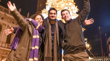 Three travellers dressed warmly standing in front of a Christmas Tree