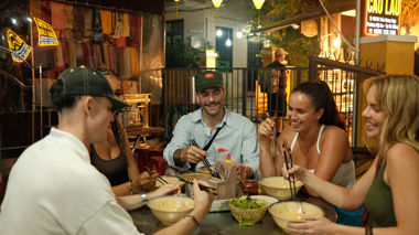 Friends laughing, eating food at a night market, Hoi An, Vietnam