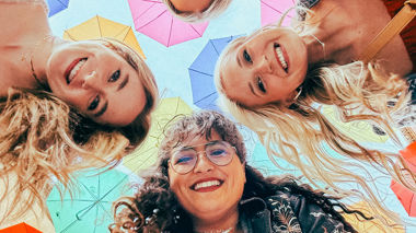 Four travellers looking down into the camera under colourful umbrellas in Barcelona, Spain