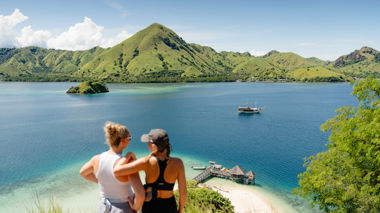 Two travellers at the top of Kelor Island, looking at the view of the sea and surrounding islands in Komodo National Park, Indonesia
