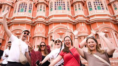 Five happy travellers standing with their arms up in the air in front of a local building in Delhi, India