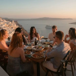 Contiki travellers gather for an evening meal overlooking Santorini's iconic whitewashed villages and sparkling Aegean Sea - Best of Greece Tour