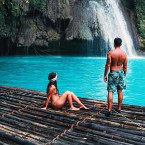 Two travellers on a bamboo raft at the base of Kawasan Falls with vivid turquoise water in Cebu Philippines - Philippines Island Hopping East Tour