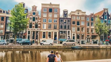 Two Travellers sitting on a canal looking at the gable houses Amsterdam, Netherlands