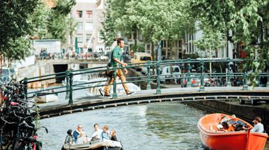 Travellers crossing a bridge over a boat in the canals of Amsterdam, Netherlands