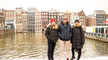 Travellers stood in front of a canal and gable houses during winter in Amsterdam, Netherlands