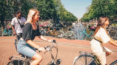 Travellers cycling over a canal bridge in Amsterdam, Netherlands