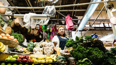 A woman stands behind a vibrant market stall of produce, Mexico City, Mexico