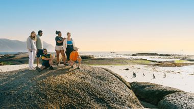 Travellers sitting on a boulder, admiring the penguins at Boulder Beach in Cape Town, South Africa