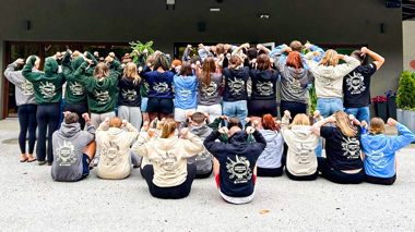 A large group of travellers facing away from the camera, showing the design on the back of their hoodie or t shirt