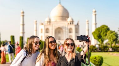 Three travellers taking a selfie with the Taj Mahal in the background in Agra, India