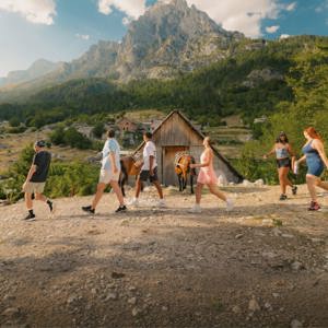 Travellers walk through a mountain village surrounded by rugged peaks and forest on the Contiki Albania: Beaches & Mountains Tour