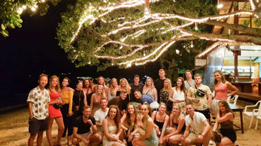 Group of travellers standing under a tree filled with lights in Koh Pha Ngan, Thailand