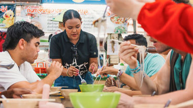 A group of travellers sitting at a table with a local enjoying traditional Thai food in Phuket, Thaialand