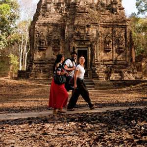Young travellers walking past an ancient Khmer stone temple in the Angkor Archaeological Park Siem Reap Cambodia - Contiki Cambodia Tour