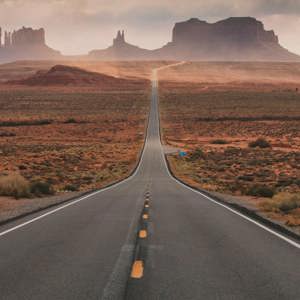 Iconic straight desert highway stretching toward the towering sandstone formations of Monument Valley Navajo Tribal Park on the Utah Arizona border USA - Contiki USA Road Trip Tour
