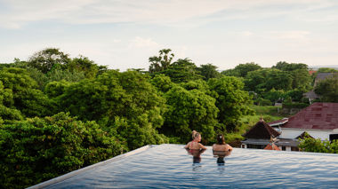Two travellers looking at trees whilst in an infinity pool in Sanur, Indonesia