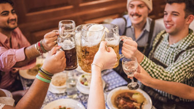 A group of travellers, at a beer hall in Munich, eating dinner and raising a stein in celebration, in Germany