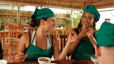 Two travellers in aprons smile while holding spring rolls, Hoi An, Vietnam