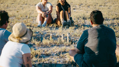 Travellers sitting down next to a meerkat in Makgadikgadi Salt Pans in Botswana, Africa