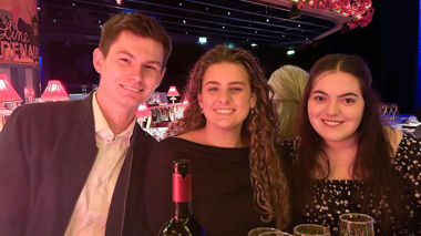 Three travellers smiling at the camera sitting at a table inside the cabaret show in Paris, France