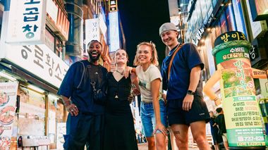 Travellers Stood Smiling in Colourful Lit Up Street in Seoul, South Korea