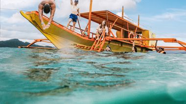 Travellers Onboard and Swimming Above and Underwater next to Yellow Boat, Port Barton Philippines