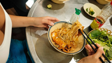 Hands holding chopsticks lifting noodles from a ceramic bowl, Hoi An, Vietnam