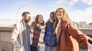 Four travellers hugging and smiling with the London Eye in the background, London, England