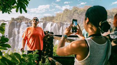 Traveller taking a photo of friend stood at view point overlooking Victoria Falls, Zambia