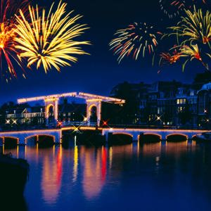 New Year's Eve fireworks lighting up the night sky over the illuminated Magere Brug bridge reflected in the Amstel River in Amsterdam Netherlands - Contiki Amsterdam New Year's Eve Tour