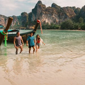 A group wading ashore from a traditional long-tail boat on a beach in Krabi - Contiki Southern Thailand: Khao Sok & Krabi Tour