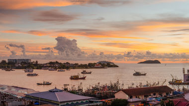 A landscape view of Kota Kinabalu, Indonesia. Buildings are in the foreground with the ocean in the background covered in boats.