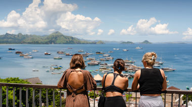 Three travellers facing away form the camera looking at boats in the ocean in Labuan Bajo, Indonesia