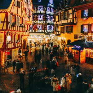 Aerial view of the festive Christmas market in France at night with illuminated half-timbered buildings and crowds of shoppers - Contiki French Christmas Markets Tour