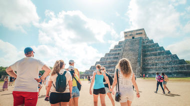 Travellers walking towards a pyramid at Chichen Itza in Mexico