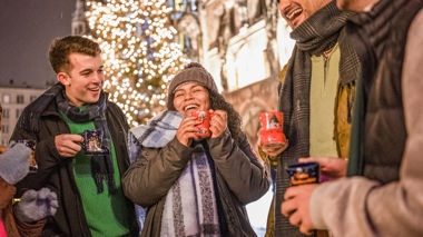Travellers standing in front of a Christmas Tree at a Christmas Market, drinking out of themed boot mugs, in Germany