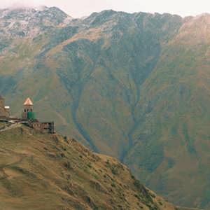 Gergeti Trinity Church sits atop a mountain ridge beneath the towering Caucasus Mountains on the Contiki Best of Georgia Tour