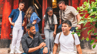 Traveller sat on steps outside building and speaking to a member of the Contiki crew, Hanoi, Vietnam