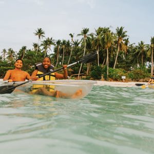 Two young travellers kayaking in a transparent kayak in crystal clear waters off a palm-lined beach in Palawan Philippines - Philippines Island Hopping West Tour