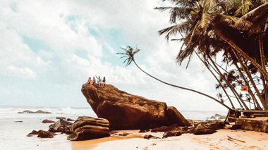 Travellers sitting on a rock on a golden beach in Koh Samui, Thailand