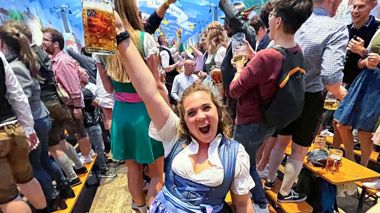 Traveller dressed wearing a dirndl, holding a stein, and standing in an Oktoberfest tent in Munich, Germany