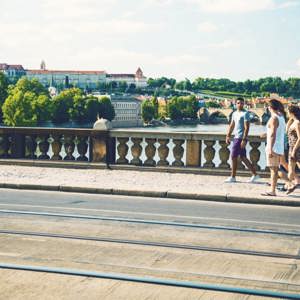 Contiki travellers walk across Prague's Charles Bridge with Prague Castle and the Vltava River in the background on the London to Rome Trail Tour