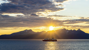 The Hurtigruten Cruise on the sea with a backdrop of mountains and sunset, Norway