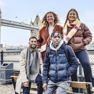 Four travellers facing the camera smiling in front of Tower Bridge and the River Thames, London, England