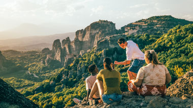 Four travellers sitting on top of a cliff admiring the view in Meteora, Greece