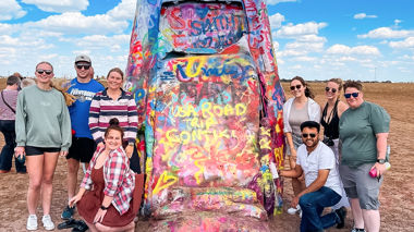 Travellers posing in front of a car at Cadillac Ranch in Amarillo, USA