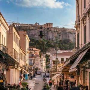 A lively street in Athens leads towards the Acropolis, with historic buildings, local shops and the ancient hilltop landmark in the distance - Greece: Ancient Wonders Tour