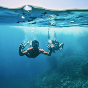 Two young travellers freediving underwater making peace signs in the clear blue waters of the Greek Islands - Contiki Athens and Santorini island hopper Tour